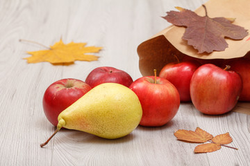 Ripe pear and red apples with paper bag on wooden desk.