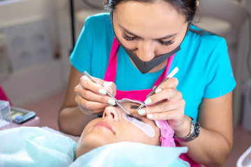 Woman master in the beauty salon work on eyelash extension to the client. Process of working as a professional stylist for lengthening eyelashes