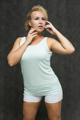 Photo portrait above the knee of a beautiful girl blonde woman with short curly hair on a gray background in bright linen is talking and showing a lot of emotions. An experienced model shows hands.