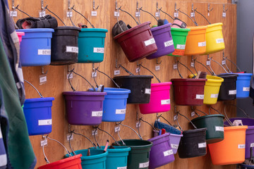Rows of color buckets with tools for horse grooming on a barn wall.