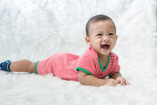 smile baby boy is shooting in the studio. fashion image of baby and family. Lovely baby lie down on a soft white carpet. 