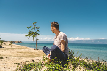 Naklejka na ściany i meble Man traveler relaxing on the beach of Olkhon island overlooking the water of the lake and the mountains and the blue sky