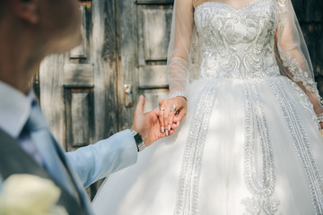 Wedding couple in love is walking outdoors. Groom in blue suit and bride in luxury dress are near the wooden wall. Beautiful bouquet in hands. Rustic style.