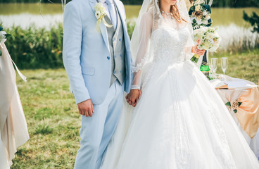 Couple is walking at the wedding ceremony outdoors. Bride and groom holding arms. Arch with flowers.