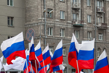 A large number of Russian flags in tricolor with stripes of white, blue and red against the background of the walls of buildings with gray windows during a rally or parade