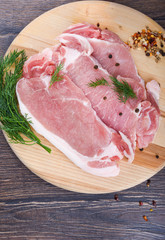 Pork steaks on a wooden cutting board with dill and spices. Raw pork meat for steaks.