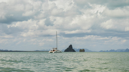 Obraz premium Small white yacht or boat near the isolated rock in the middle of the wide open wavy sea amid cloudy weather