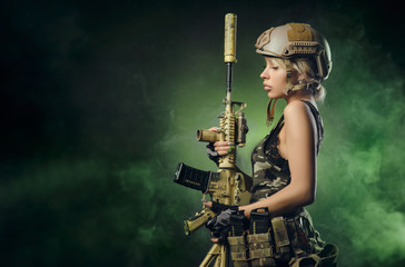the girl in military overalls airsoft posing with a gun in his hands on a dark background in the...