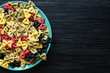 Multicolor italian raw pasta close-up in a ceramic plate on the dark wooden table. Top view