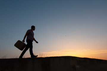 silhouette of man with suitcase at sunrise