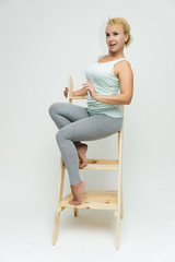 Full-length portrait of a slim beautiful pretty girl blonde woman with short curly hair on a white background in bright fitness clothes sitting on the stairs in various poses and a lot of emotions.