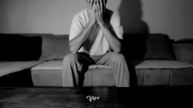 Depressed man suffering from suicidal depression want to commit suicide by overdose taking strong medicament drugs and pills pain killers sitting in his dark room selective focus moody dramatic look