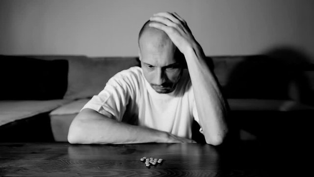 Depressed man suffering from suicidal depression want to commit suicide by overdose taking strong medicament drugs and pills pain killers sitting in his dark room selective focus moody dramatic look