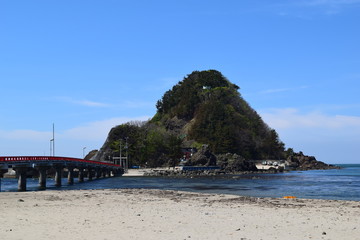 Fototapeta na wymiar 白山島（東北の江ノ島）／ 山形県鶴岡市の由良海岸沖にある白山島は、「日本の渚百選」と、「快水浴場百選」に選ばれた由良海岸のシンボル的な島で、その景観から「東北の江ノ島」と呼ばれています。由良海岸から島までは赤い白山橋が架けられており、歩いて島に渡ることが出来ます。