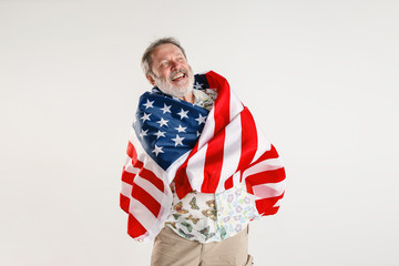 Celebrating an Independence day. Stars and Stripes. Senior man with the flag of the United States of America isolated on white studio background. Looks crazy happy and proud as a patriot of his