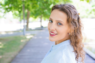 Relaxed happy girl enjoying nature in park. Headshot of young woman with wavy hair looking at...