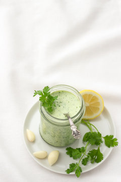 Yoghurt cilantro sauce with garlic and olive oil in a glass jar on a white background, selective focus, vertical	