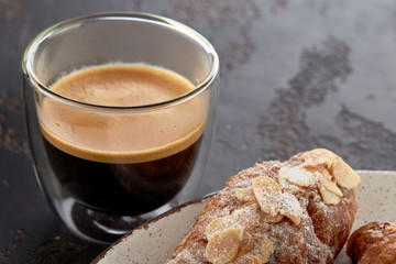 Cup of espresso and an almond croissant on a plate close-up. Delicious breakfast.