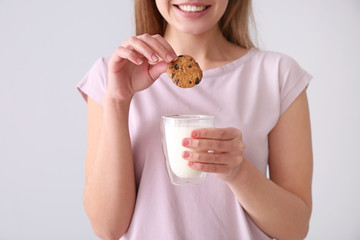 Beautiful young woman with tasty cookie and glass of milk on light background