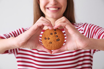 Beautiful young woman with tasty cookie on light background, closeup