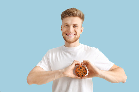Handsome young man with tasty cookie on color background