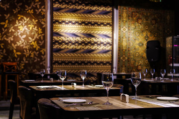 Empty wine glasses and tableware close up view on wooden table in restaurant with silk rugs on the wall
