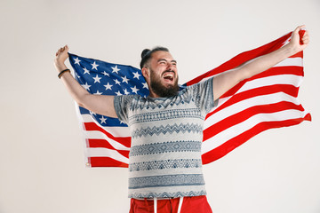 Celebrating an Independence day. Stars and Stripes. Young man with the flag of the United States of America isolated on white studio background. Looks crazy happy and proud as a patriot of his country