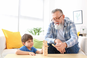 Cute little boy playing with grandfather at home