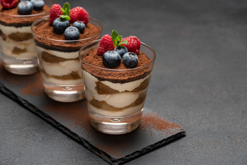 Classic tiramisu dessert with blueberries and raspberries in a glass on stone serving board on dark concrete background