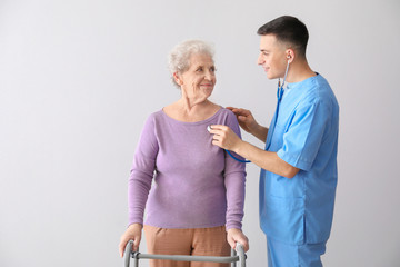 Fototapeta premium Young caregiver with senior woman on grey background