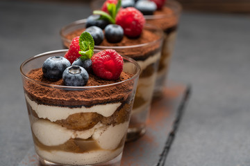 Classic tiramisu dessert with blueberries and raspberries in a glass on stone serving board on dark concrete background