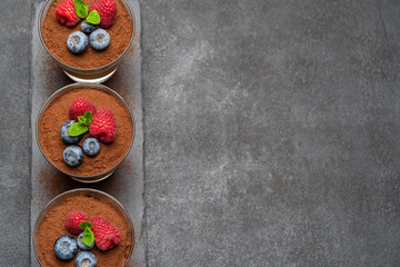 Classic tiramisu dessert with blueberries and raspberries in a glass on stone serving board on dark concrete background