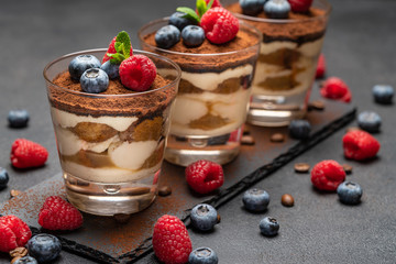 Classic tiramisu dessert with blueberries and raspberries in a glass on stone serving board on dark concrete background - obrazy, fototapety, plakaty