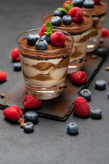 Classic tiramisu dessert with blueberries and raspberries in a glass on stone serving board on dark concrete background
