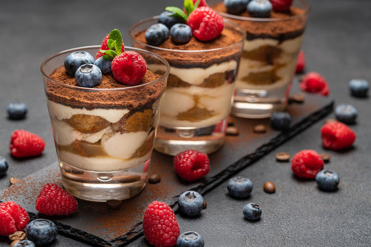 Classic tiramisu dessert with blueberries and raspberries in a glass on stone serving board on dark concrete background