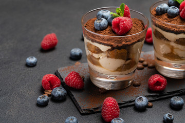 Classic tiramisu dessert with blueberries and raspberries in a glass on stone serving board on dark concrete background
