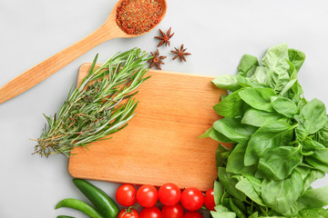 Wooden board with fresh herbs, vegetables and spices on light background