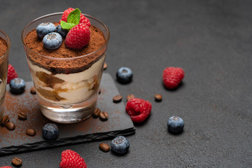 Classic tiramisu dessert with blueberries and raspberries in a glass on stone serving board on dark concrete background