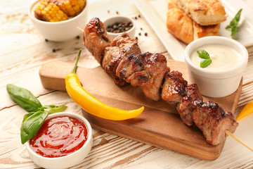 Board with tasty grilled meat and sauces on wooden table