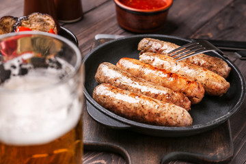 Frying pan with tasty grilled sausages and beer on wooden table