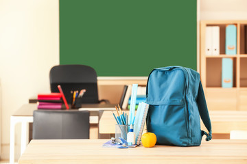 School backpack with stationery on table in classroom