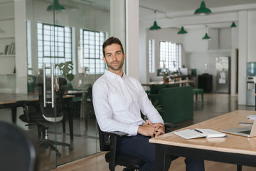 Confident young businessman sitting at his desk in an office