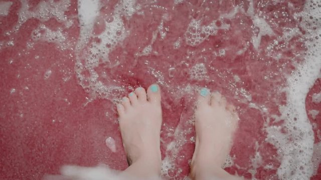 Waves wash women's feet on the bard dark red sand by the sea ocean, relaxation, enjoyment of rest, vacation, tourist trip, travel, close-up, slow motion