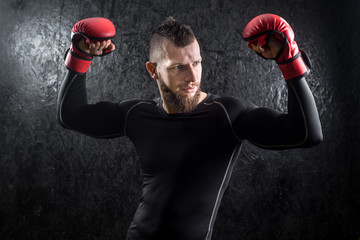An athletic man wearing red kickboxing gloves posing and ready to fight in the gym