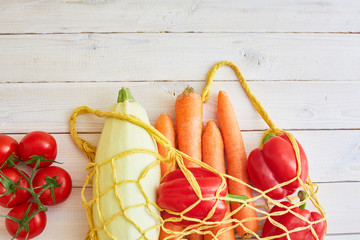 String bag with various fresh vegetables on white textured background. Organic eco bio products...