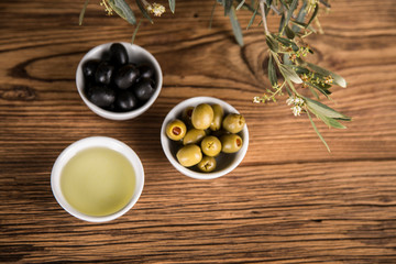 Olive oil, olive tree and green and black olives on a wooden table