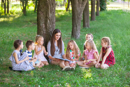 children hold a lesson with the teacher in the park on a green lawn.