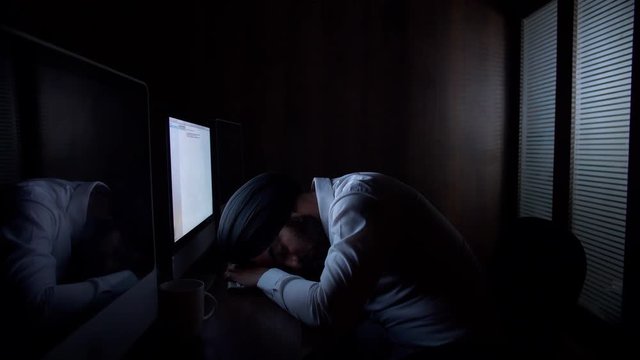 Young Indian office employee sleeping on the desk  working late night - office employee. Indian stock footage of a tired employee sleeping in front of the computer due to late night work 