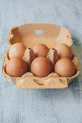 Close up view of raw chicken eggs in egg box on white wooden table. 