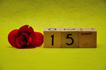15 August on wooden blocks with a red flower on a yellow background